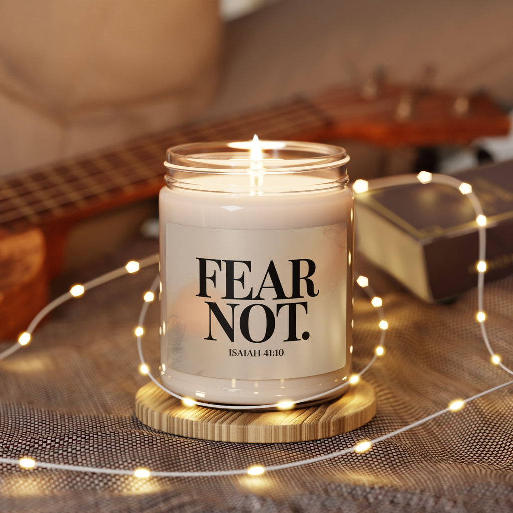 Candle in a jar with 'FEAR NOT' text on a wooden coaster surrounded by string lights and a guitar in the background.