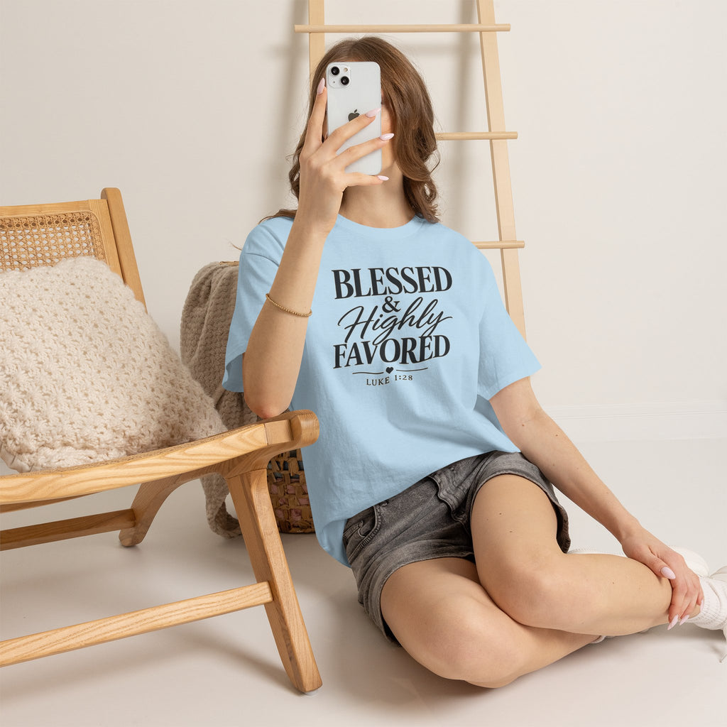 Person wearing a light blue t-shirt with 'Blessed & Highly Favored' text, sitting on the floor.