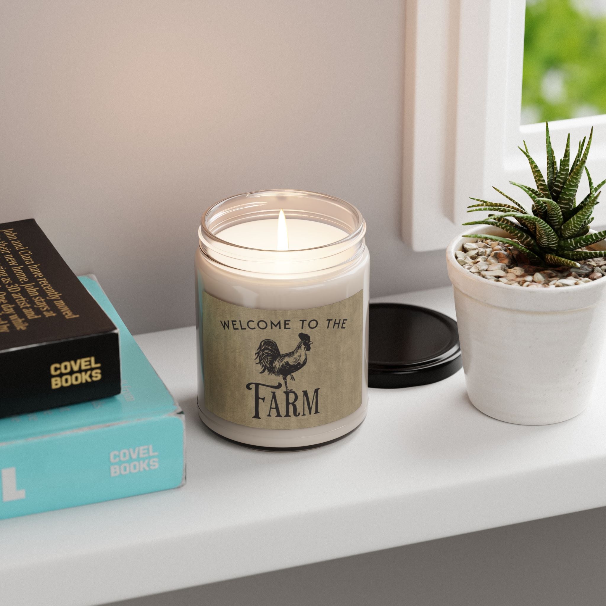 Candle with 'Welcome to the Farm' text on a shelf with books and a plant