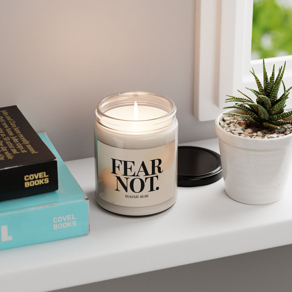 Candle with 'FEAR NOT' text on a shelf with books and a plant
