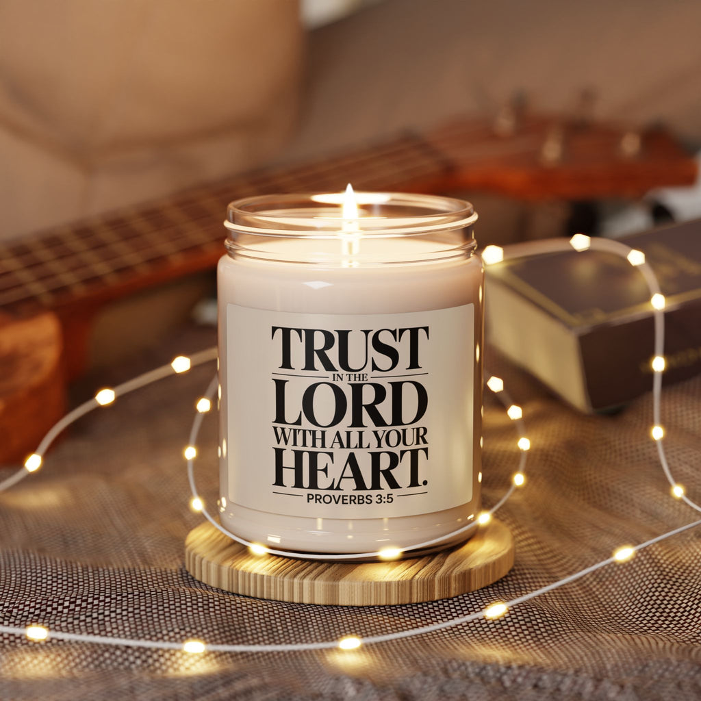 Candle in a jar with a motivational quote on a wooden coaster surrounded by string lights and a guitar in the background.